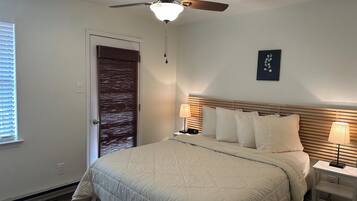 A bedroom with a bed, ceiling fan, bedside lamps, and a door with a window.