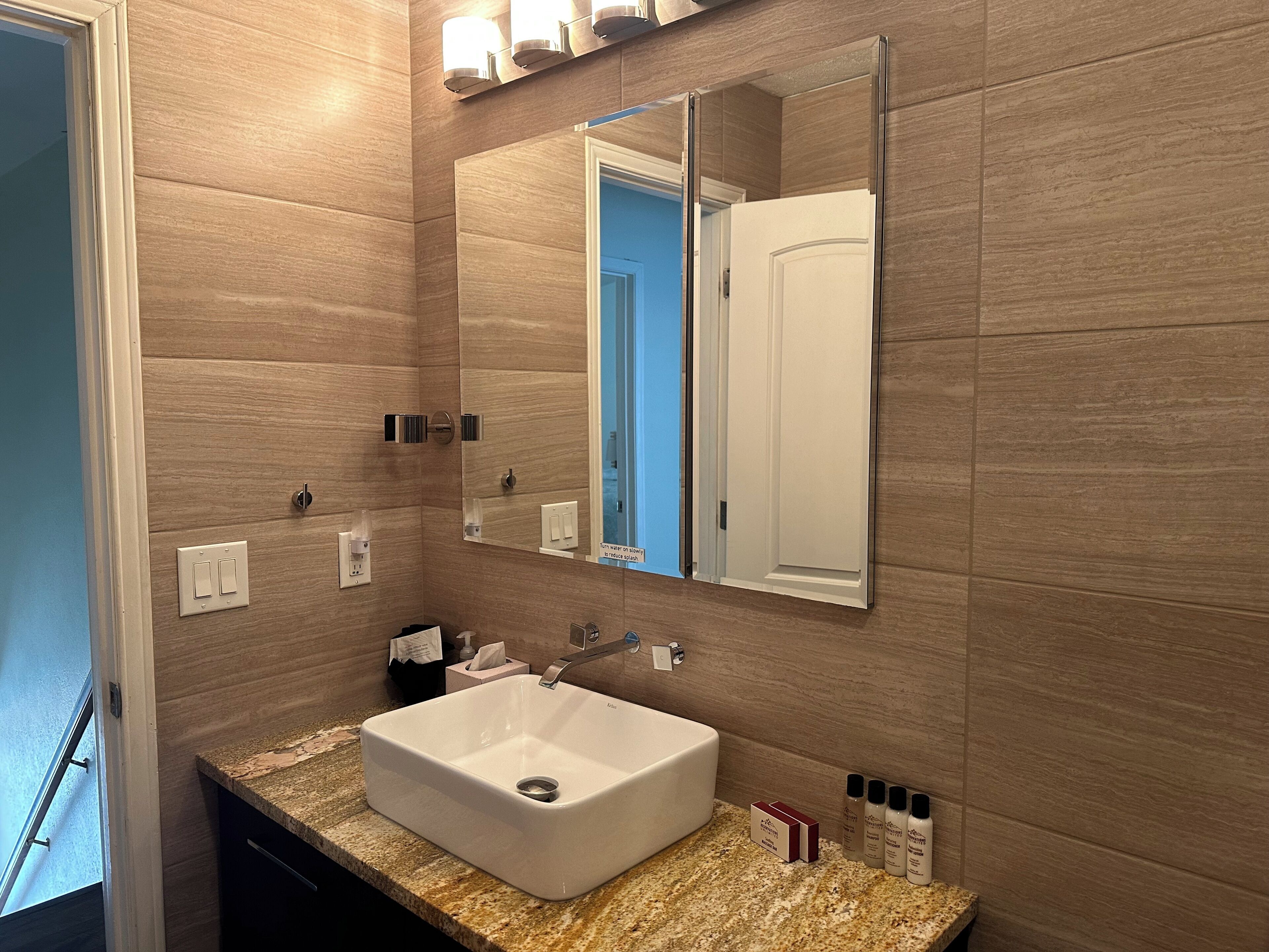 A bathroom with a white sink, a mirror, and a towel dispenser.