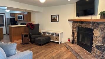 A living room with a fireplace, a television, a kitchen in the background, and a stone accent wall.