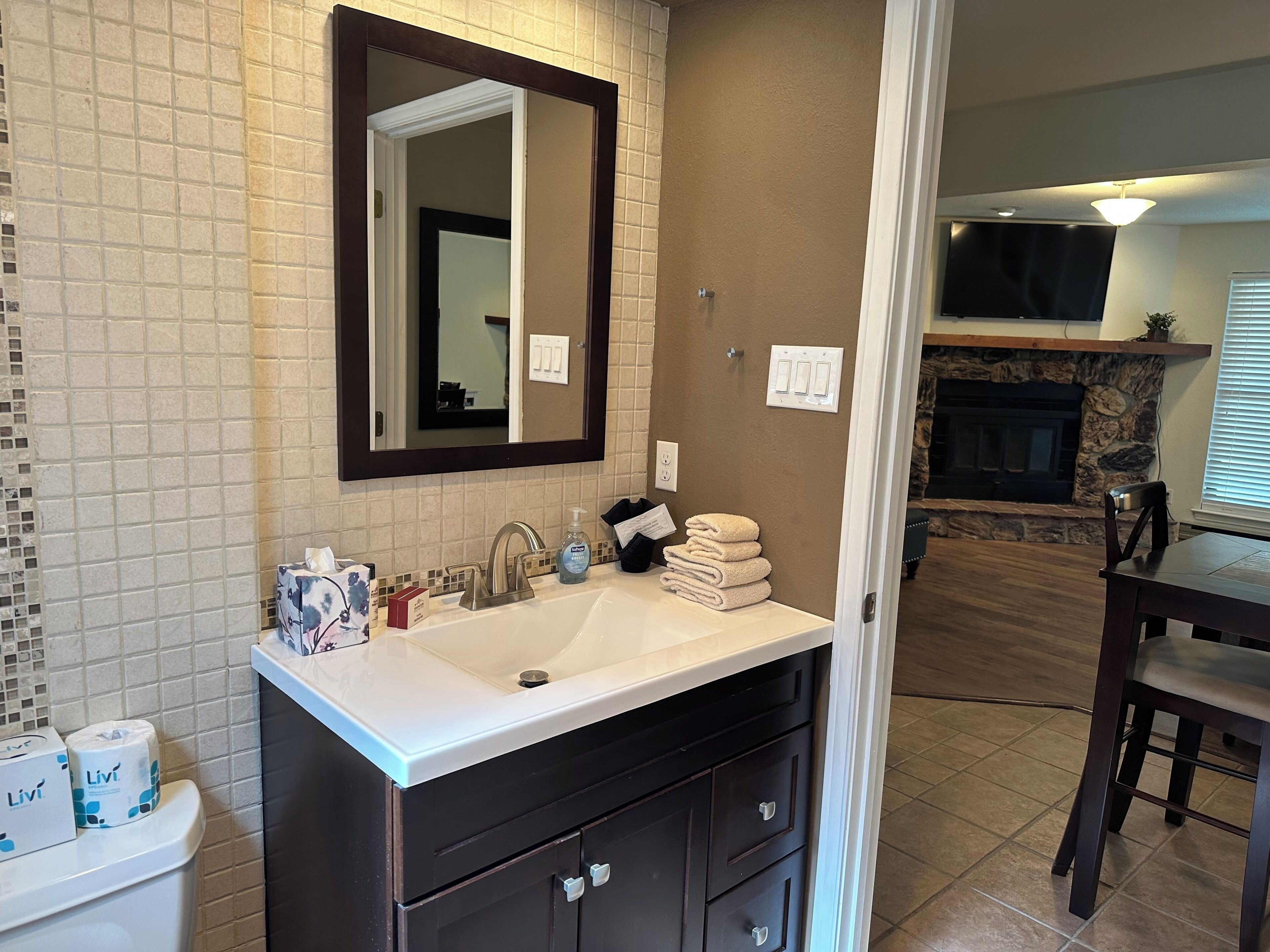 A bathroom with a white sink, dark cabinetry, a mirror, and a tiled wall.