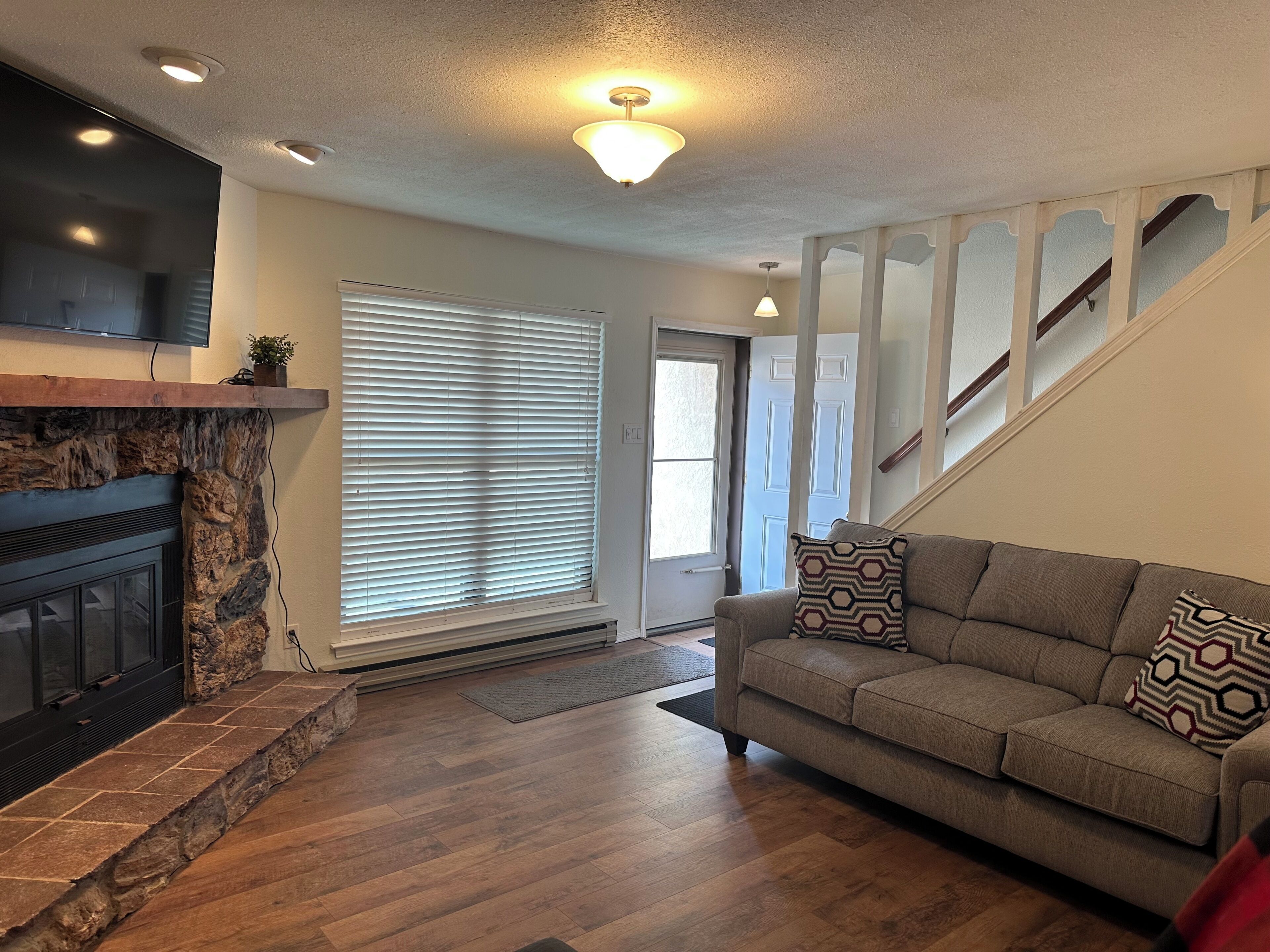 A living room with a fireplace, a sofa, a staircase, and a door leading outside.