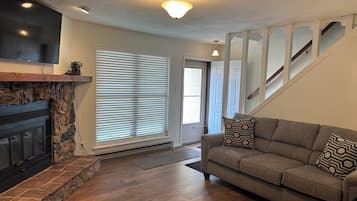 A living room with a fireplace, a sofa, a staircase, and a door leading outside.