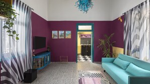 A living room with a teal sofa, a TV on a blue cabinet, and a purple wall. - Eclectic1BR in Talpiot mkt by Sea N Rent (Haifa)