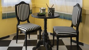 A room with yellow walls, a checkered floor, two striped chairs, a small table with a teapot and cups, and a ceiling light fixture. - Eclectic1BR in Talpiot mkt by Sea N Rent (Haifa)