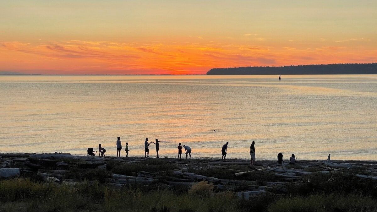 A sunset over a calm body of water with people on a rocky shore.