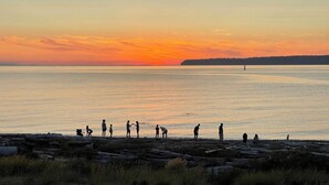 Un coucher de soleil sur une étendue d’eau calme, avec des personnes sur une plage rocheuse.