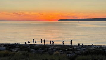 A sunset over a calm body of water with people on a rocky shore.