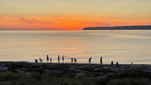 A sunset over a calm body of water with people on a rocky shore.