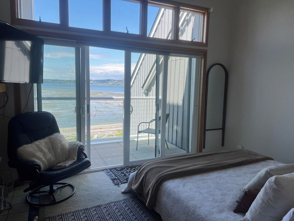 Ein Schlafzimmer mit Bett, Sessel, großem Fenster und Meerblick.
