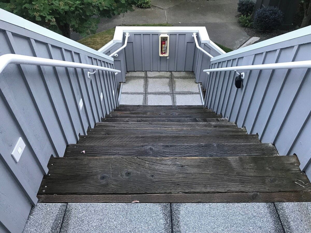 Una escalera de madera con barandillas y pasamanos de metal, que conduce a un rellano con un buzón.