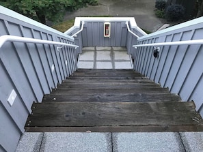 Un escalier en bois, doté de rampes et d’une main courante en métal, mène à un palier où se trouve une boîte aux lettres.