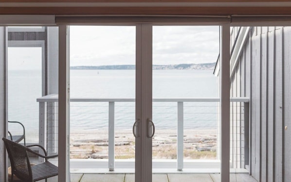 A sliding glass door leading to a balcony with a view of a body of water and distant land.