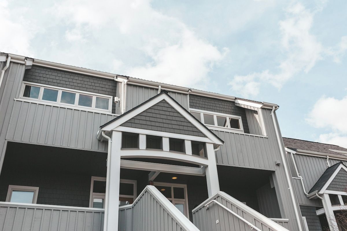 A multi-story building with a grey exterior, white trim, and a central entrance with a ramp.