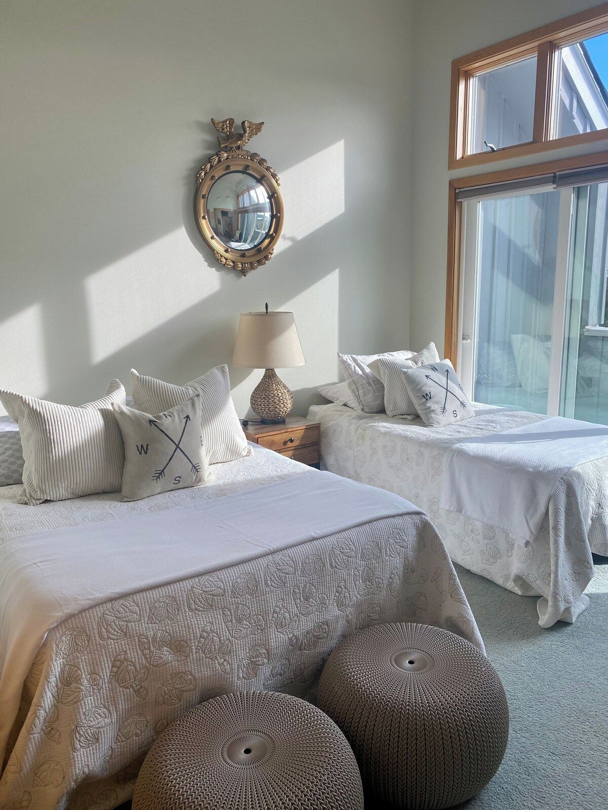 A bedroom with two beds, a mirror, a lamp, and a large window.