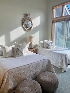 A bedroom with two beds, a mirror, a lamp, and a large window.