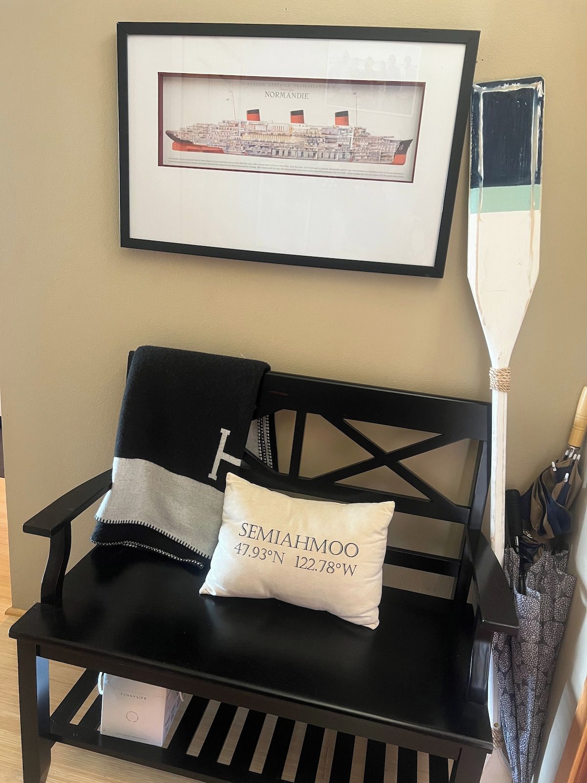 A black chair with a pillow labeled 'SEMAHMOO 47.93°N 122.78°W' and a framed picture of a ship on the wall.