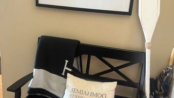 A black chair with a pillow labeled 'SEMAHMOO 47.93°N 122.78°W' and a framed picture of a ship on the wall.