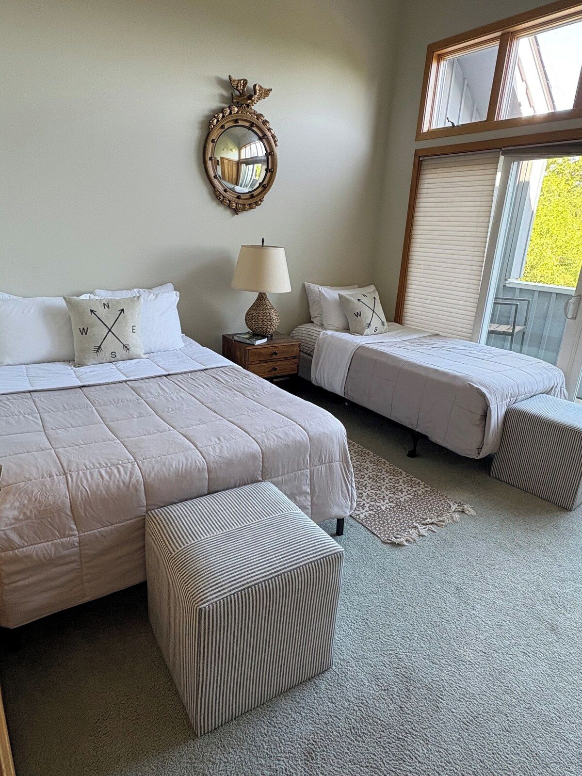 A bedroom with two beds, a nightstand, a lamp, a mirror, and a window with blinds.
