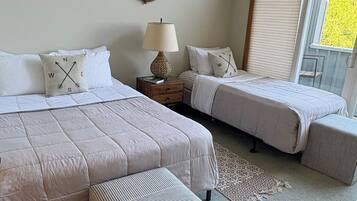 A bedroom with two beds, a nightstand, a lamp, a mirror, and a window with blinds.