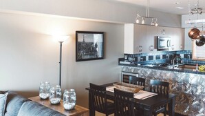 Une cuisine moderne dotée d’un îlot central, d’appareils électroménagers en acier inoxydable et d’un luminaire suspendu.