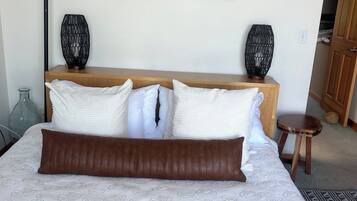 A bedroom with a bed, pillows, a nightstand, a lamp, a painting, and a door.
