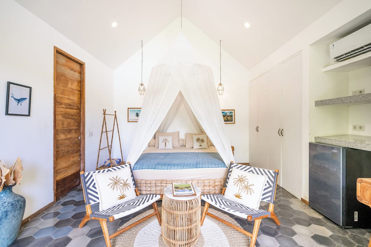 A bedroom with a canopy bed, a small round table, two chairs, a ladder, and a refrigerator.
