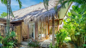 A tropical villa with a thatched roof, bamboo fence, and lush greenery. - Ohana Bungalow by Betterplace  (Canggu)