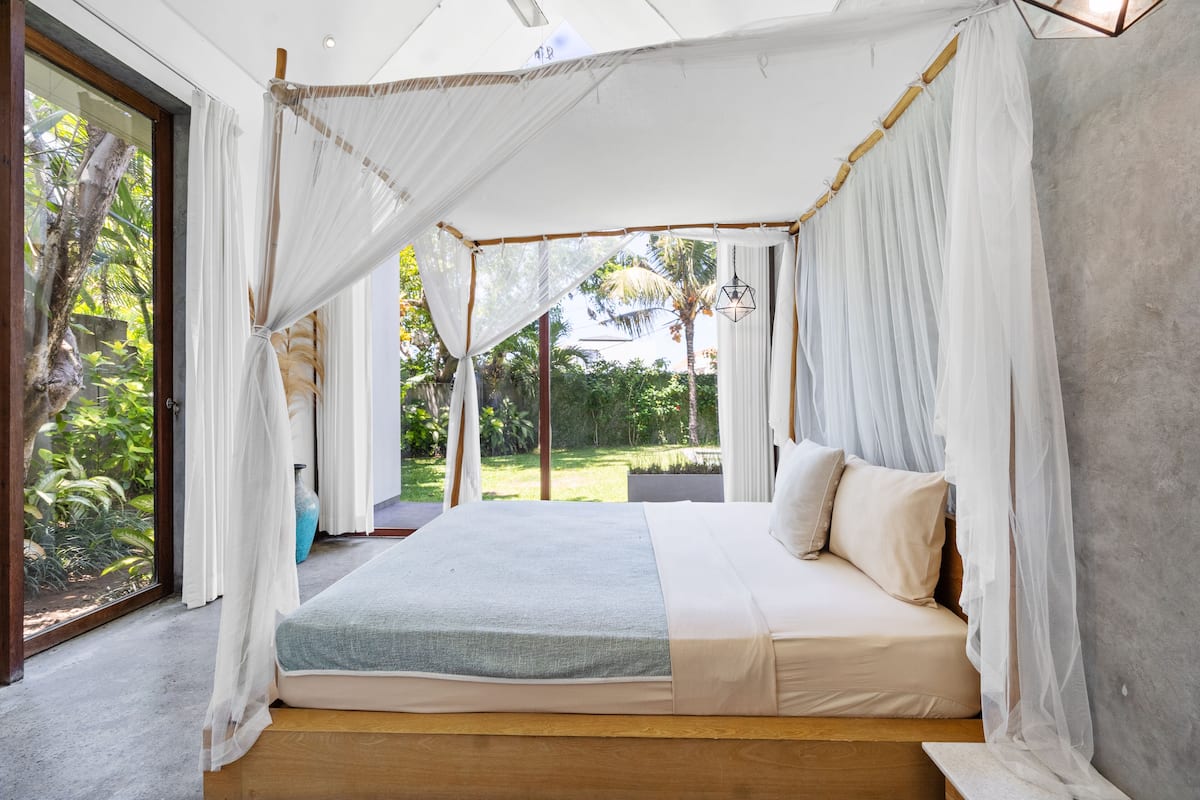A bedroom with a canopy bed, large windows, and a view of greenery.