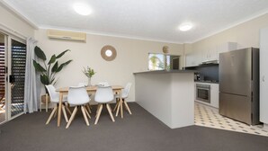 Una cocina compacta con refrigerador, horno y una zona de comedor con mesa y sillas.