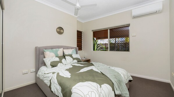 Un dormitorio con una cama, ventilador de techo, aire acondicionado, ventana con vistas y un reloj de pared.