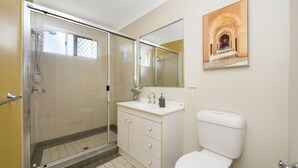 Un baño con cabina de ducha de vidrio, un lavamanos blanco con espejo y un inodoro.