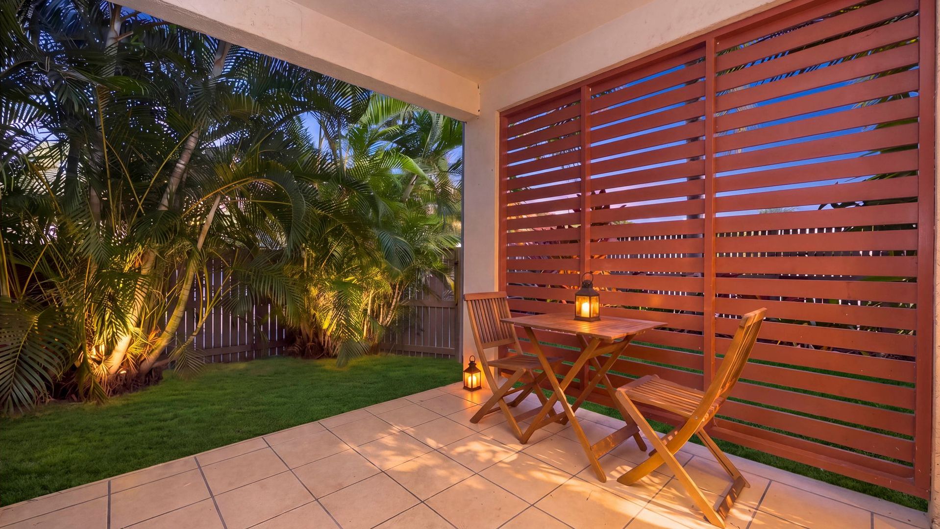 An outdoor patio with a table and chairs, a wooden fence, and palm trees.