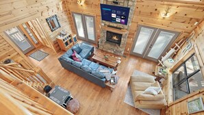 En stuga med träpanel på insidan, en steneldstad, en soffa, ett soffbord och en tv som är monterad på väggen.