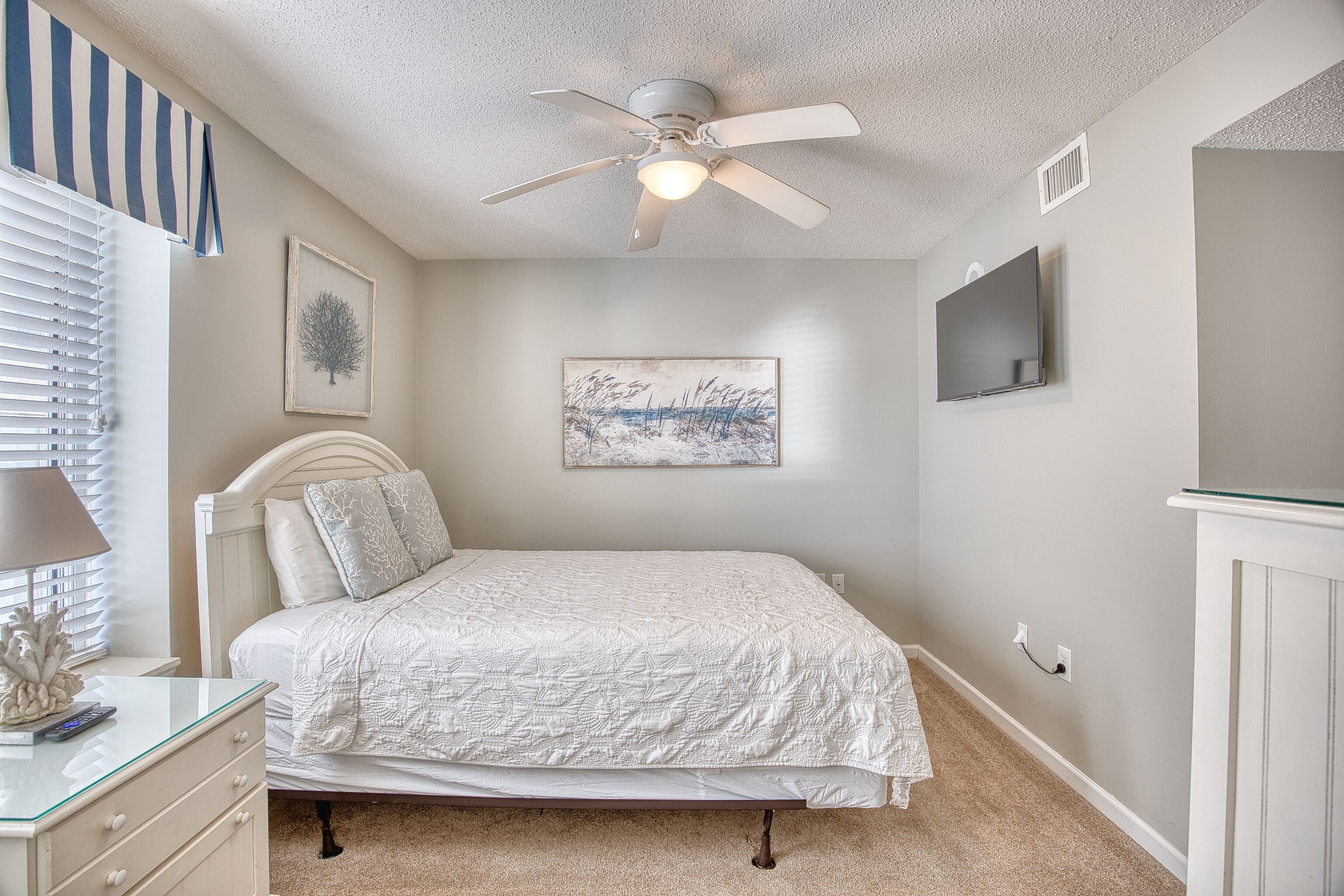 A bedroom with a bed, a ceiling fan, a TV, and artwork on the walls.