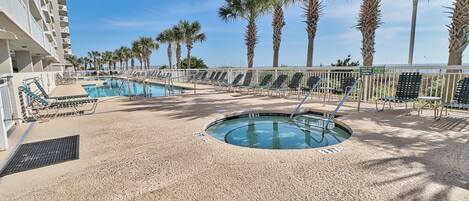 Zona de piscina con sillones reclinables, un jacuzzi y palmeras.