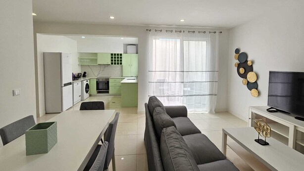 Una sala moderna con sofá, mesa de comedor y cocina al fondo.
