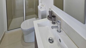 Un baño moderno con lavamanos blanco, inodoro y ducha con cerramiento de vidrio.