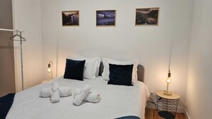 Una cama bien tendida con ropa de cama blanca y azul oscuro, dos lámparas de noche y tres cuadros en la pared.