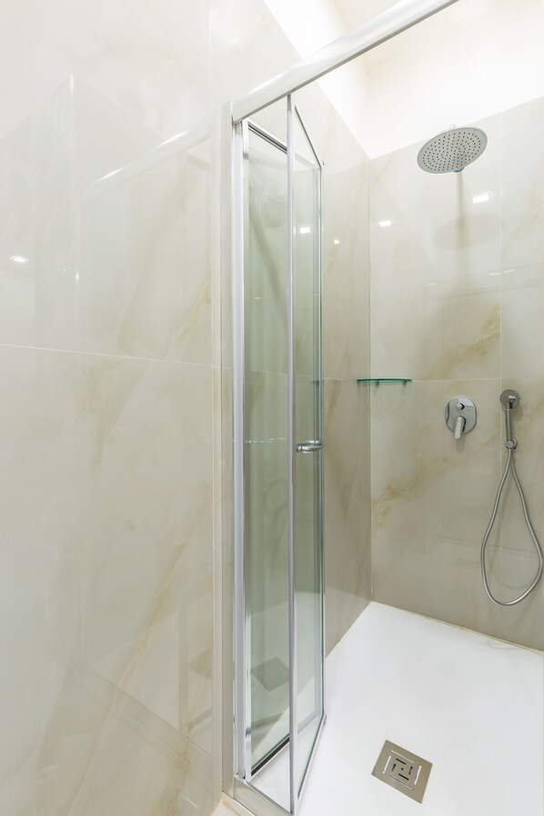 A modern shower with a glass door, a handheld showerhead, and a wall-mounted control. - Toledo house Apartments (Naples)