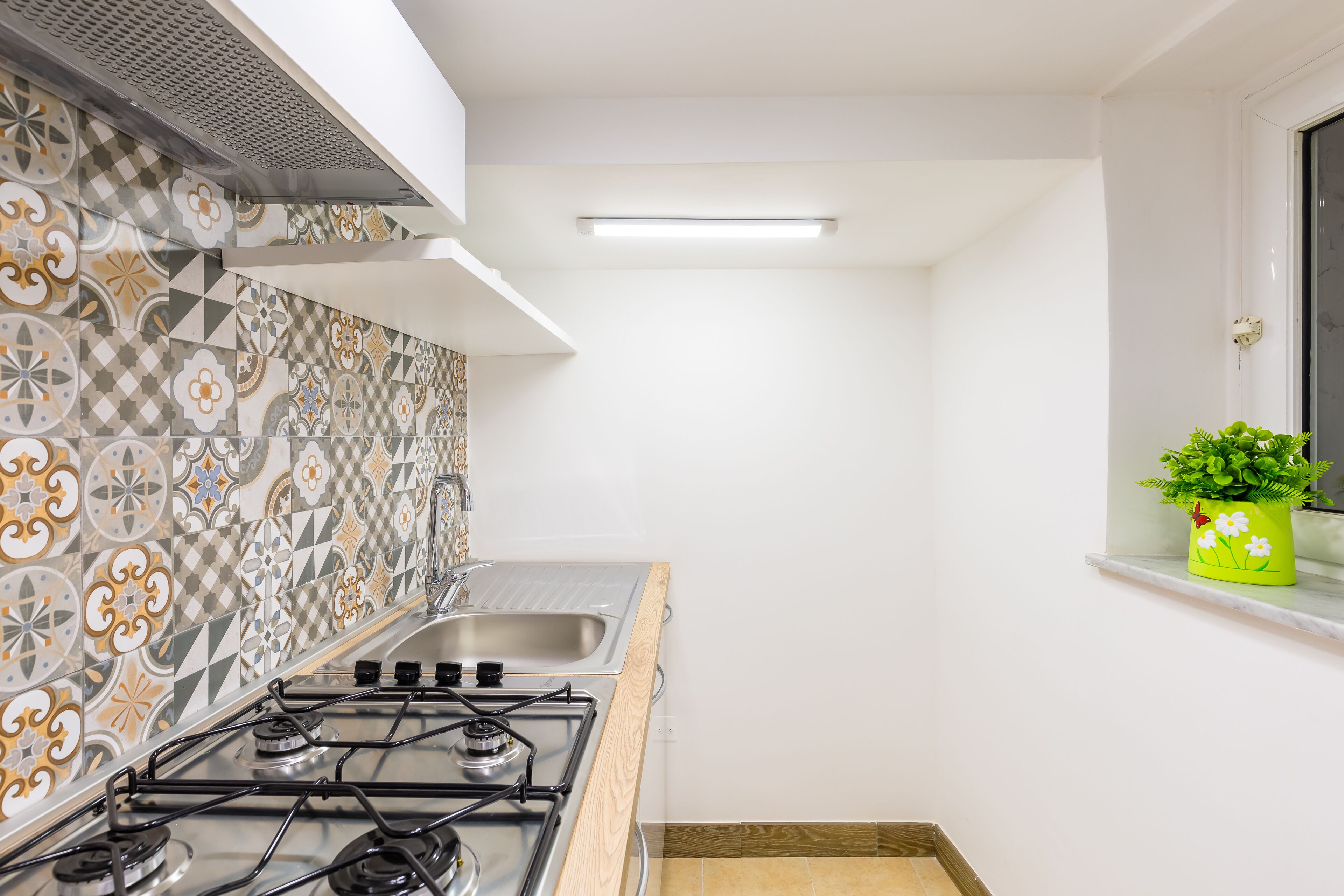 Cozinha com fogão a gás, pia e ladrilhos estampados.
