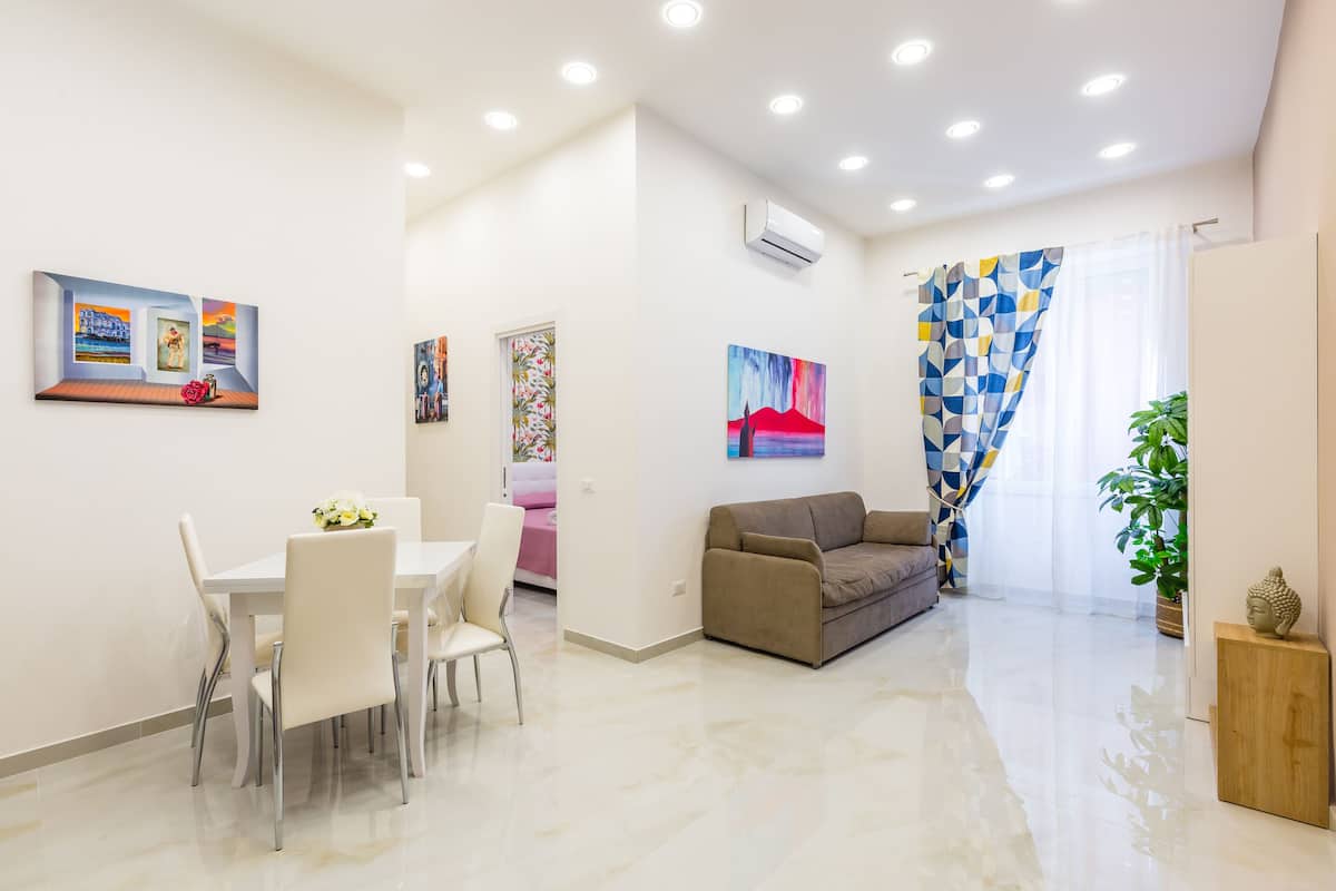A modern living room with a dining area, a sofa, and a potted plant.