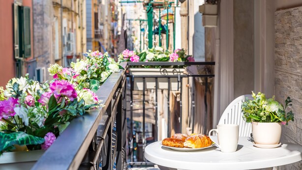 En balkon med blomster, et bord med bagværk og en potteplante.