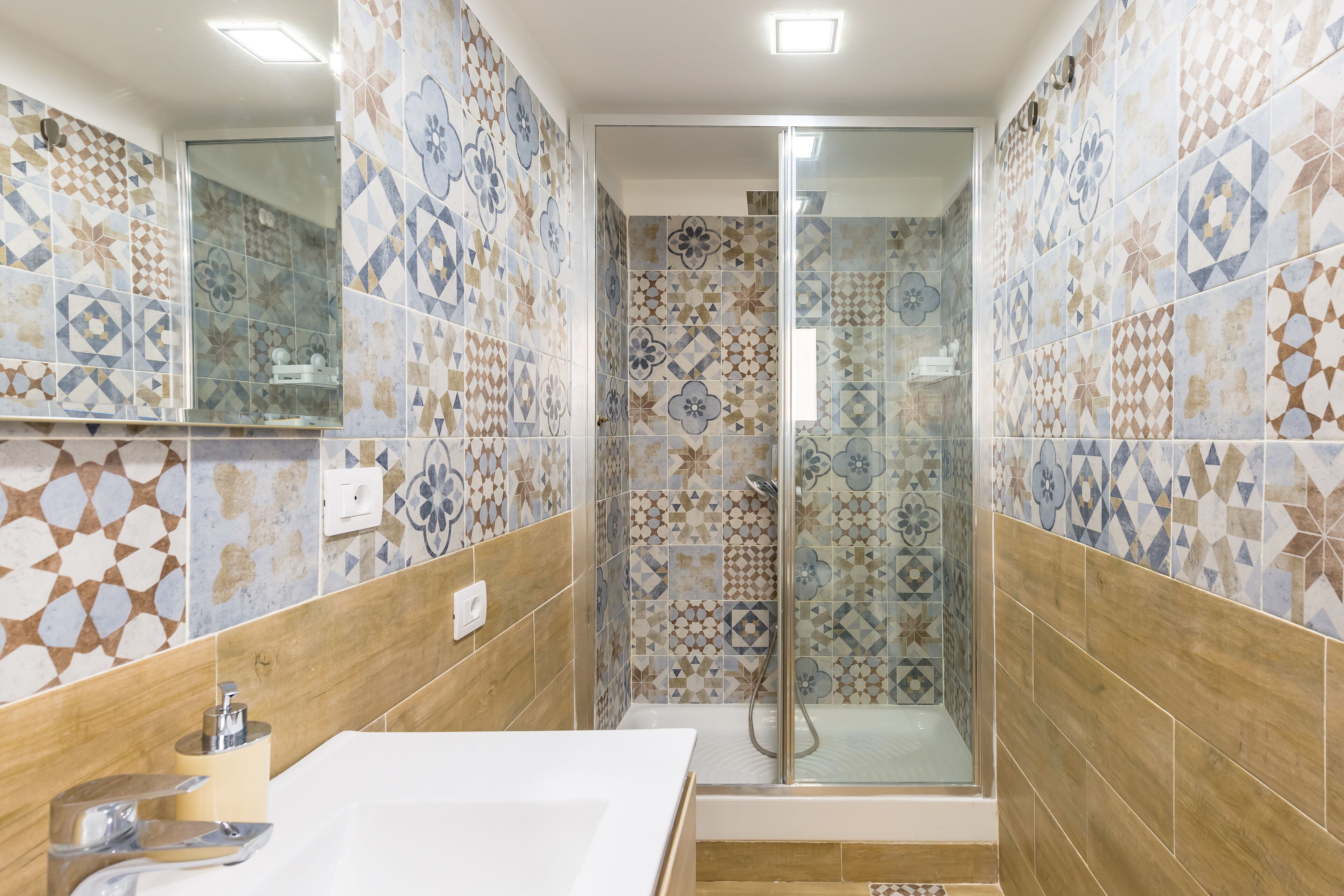A bathroom with a shower, tiled walls, a sink, and a mirror.
