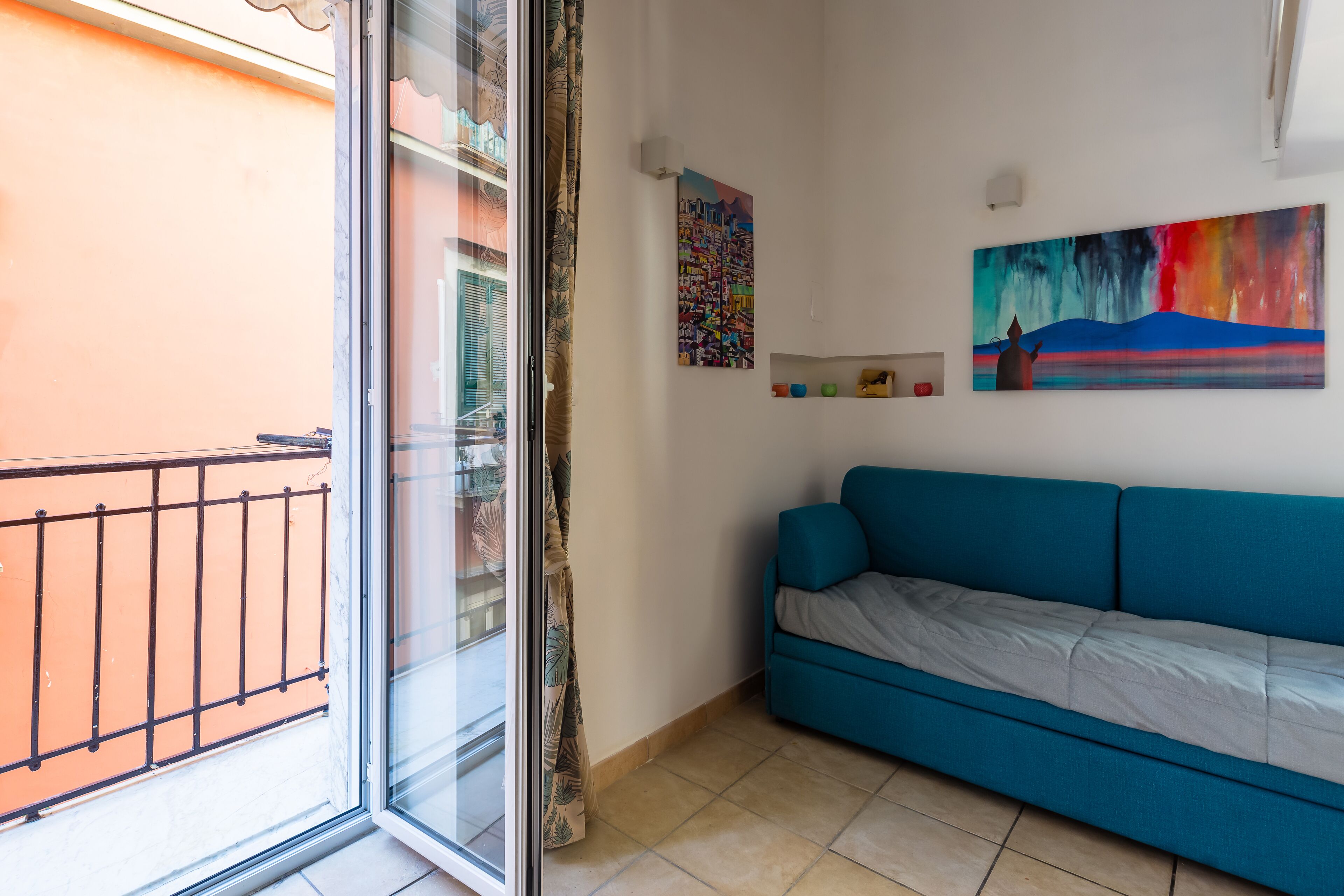 Une pièce avec un canapé bleu, une porte vitrée donnant sur un balcon et deux tableaux accrochés au mur.