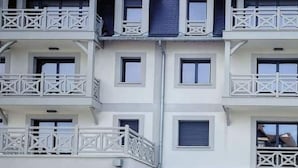 A multi-story building with a symmetrical facade, featuring balconies with white railings and a central section with a dark roof. - Standing, Centre, 2 Sdb 2 WC, Balcon, Parking (Deauville)