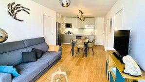 A modern living room with a grey sofa, a glass coffee table, and a television on a wooden stand. - Standing, Centre, 2 Sdb 2 WC, Balcon, Parking (Deauville)