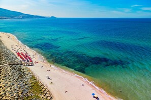 Una playa con aguas azules cristalinas, una orilla arenosa y un espigón de madera con sombrillas.