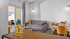 A modern living room with a grey sofa, a dining table set with yellow chairs, and a bottle of Pariglia wine. - Villa Maria – brand new villa with a garden in Valledoria (Valledoria)