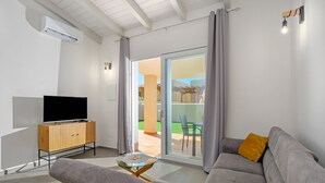A modern living room with a flat-screen TV, wooden cabinet, glass coffee table, and a grey sofa with a mustard cushion. - Villa Maria – brand new villa with a garden in Valledoria (Valledoria)