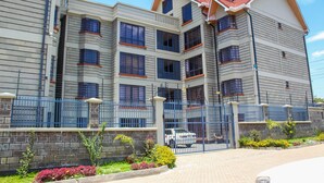A multi-story residential building with a brick facade, a gated entrance, and a driveway. - Isomer Comfort Homes (Nakuru)